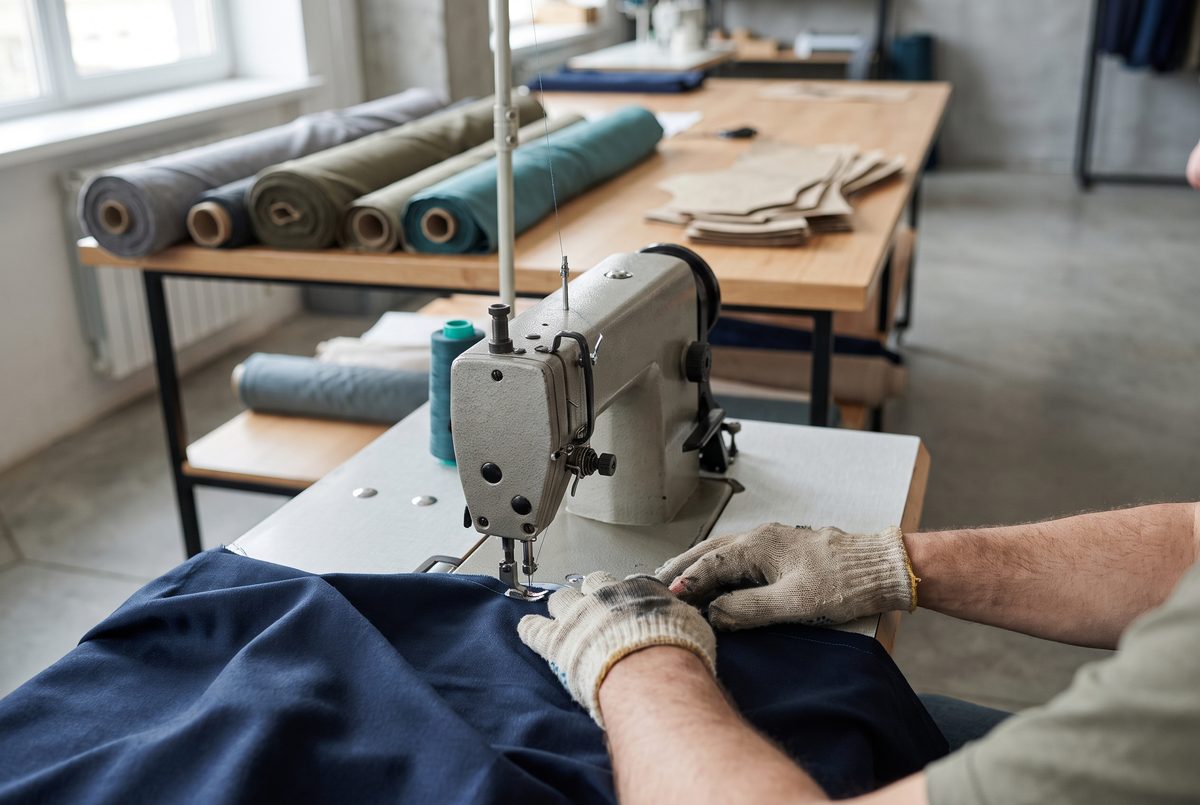 Machinist sewing navy fabric on an industrial sewing machine, fabric rolls behind